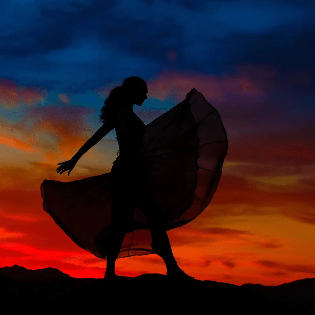 Silhouette of a woman in a flowing dress dancing against a red sunset sky