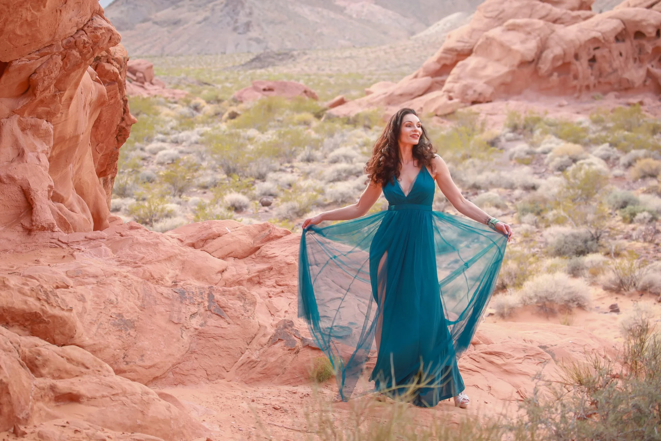 Makayla Léone in a flowing teal gown among red desert rocks
